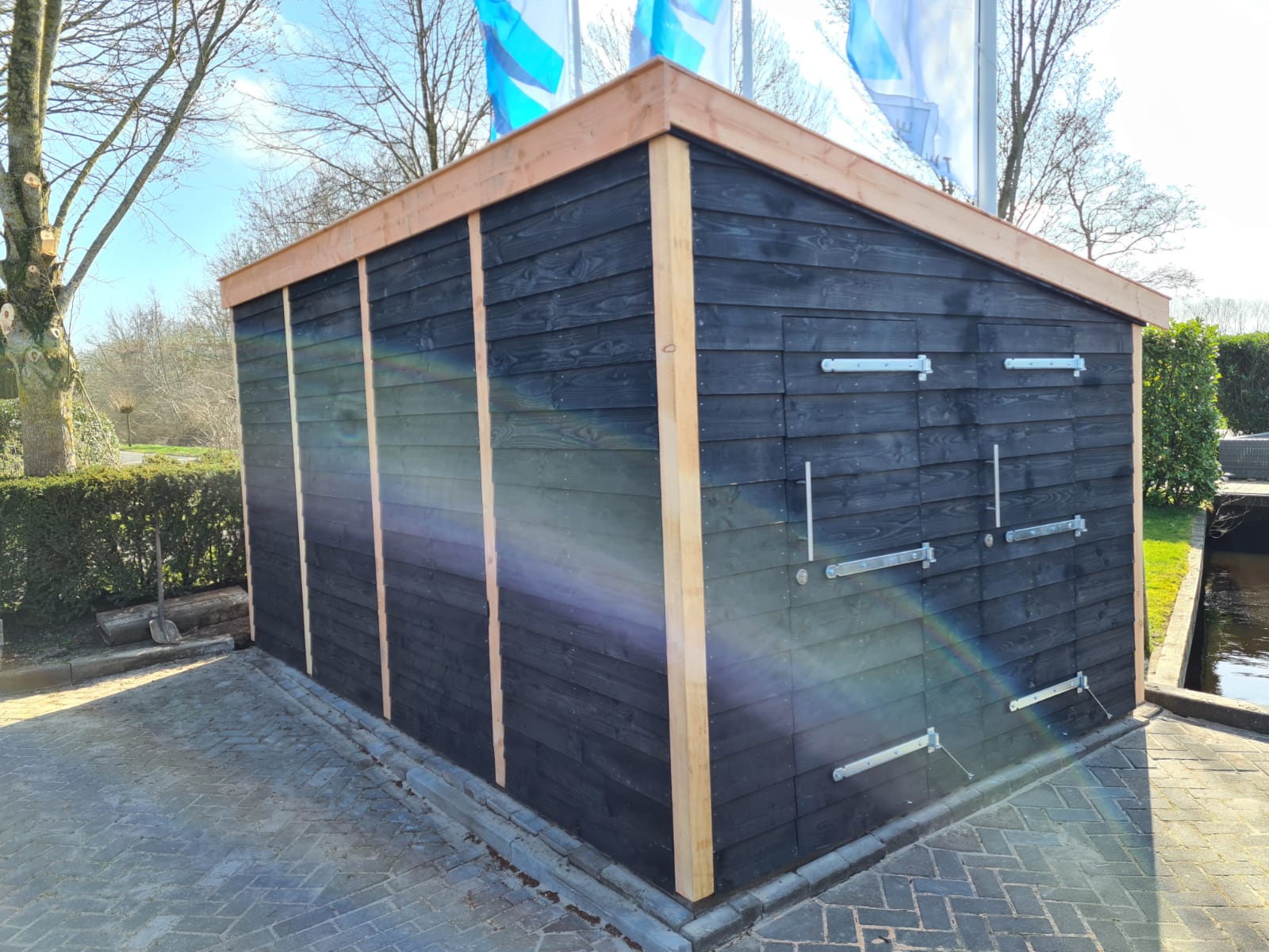 Opgeleverde berging van zwart gebeitst hout met een douglas dakrand op een nieuw bestraat terras