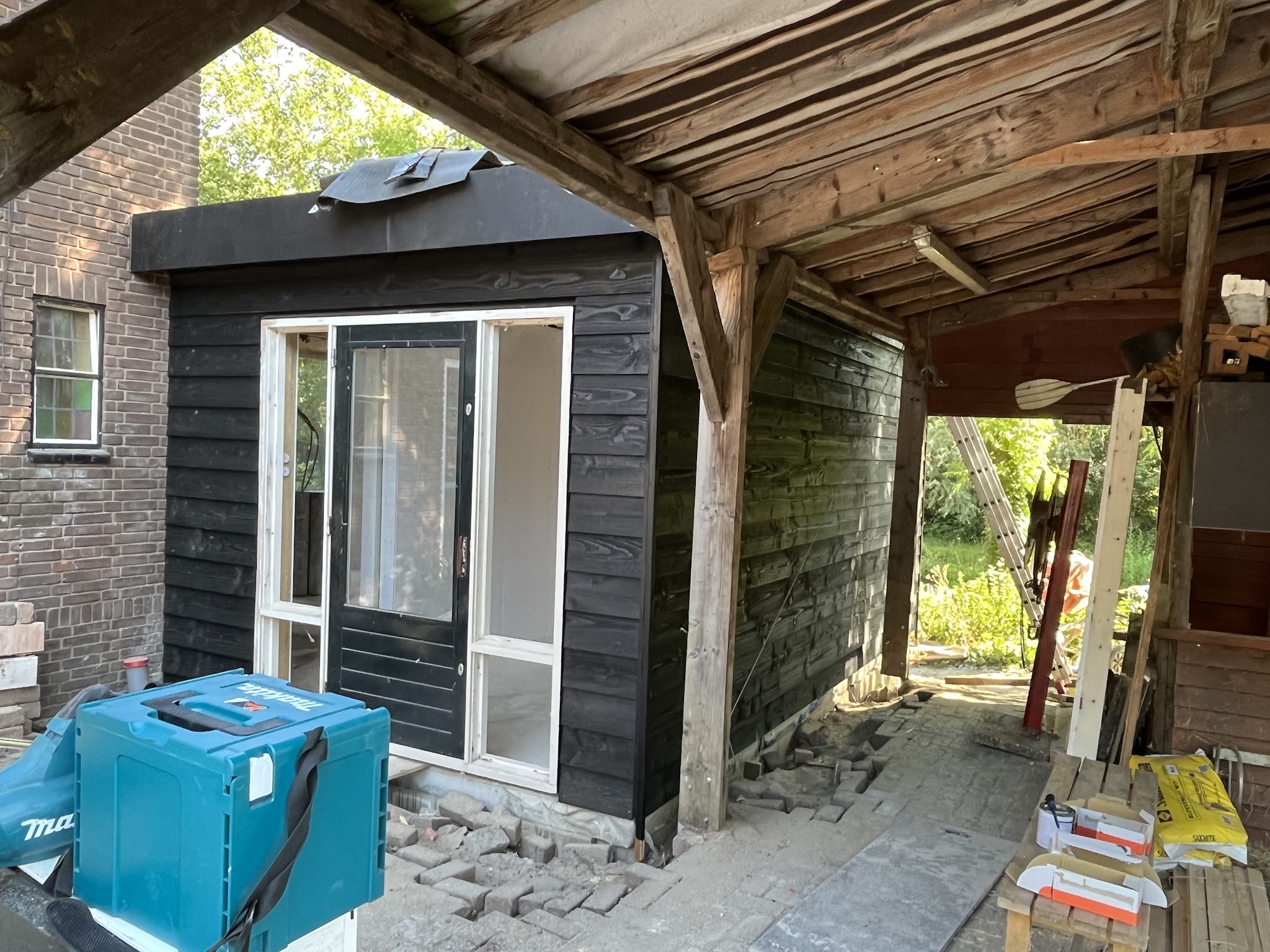 Nieuwe zwart gebeitste bijbouw met witte kozijnen, gebouwd onder een bestaande houten kapschuur