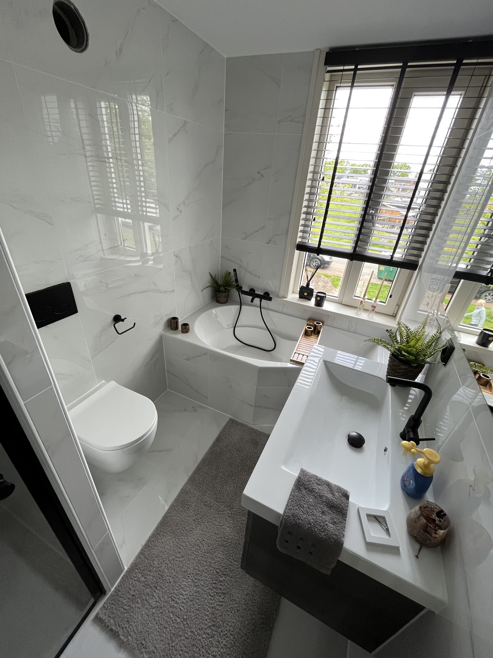 Opgeleverde badkamer met wit marmerlook tegelwerk, ligbad, wastafel en zwarte kranen