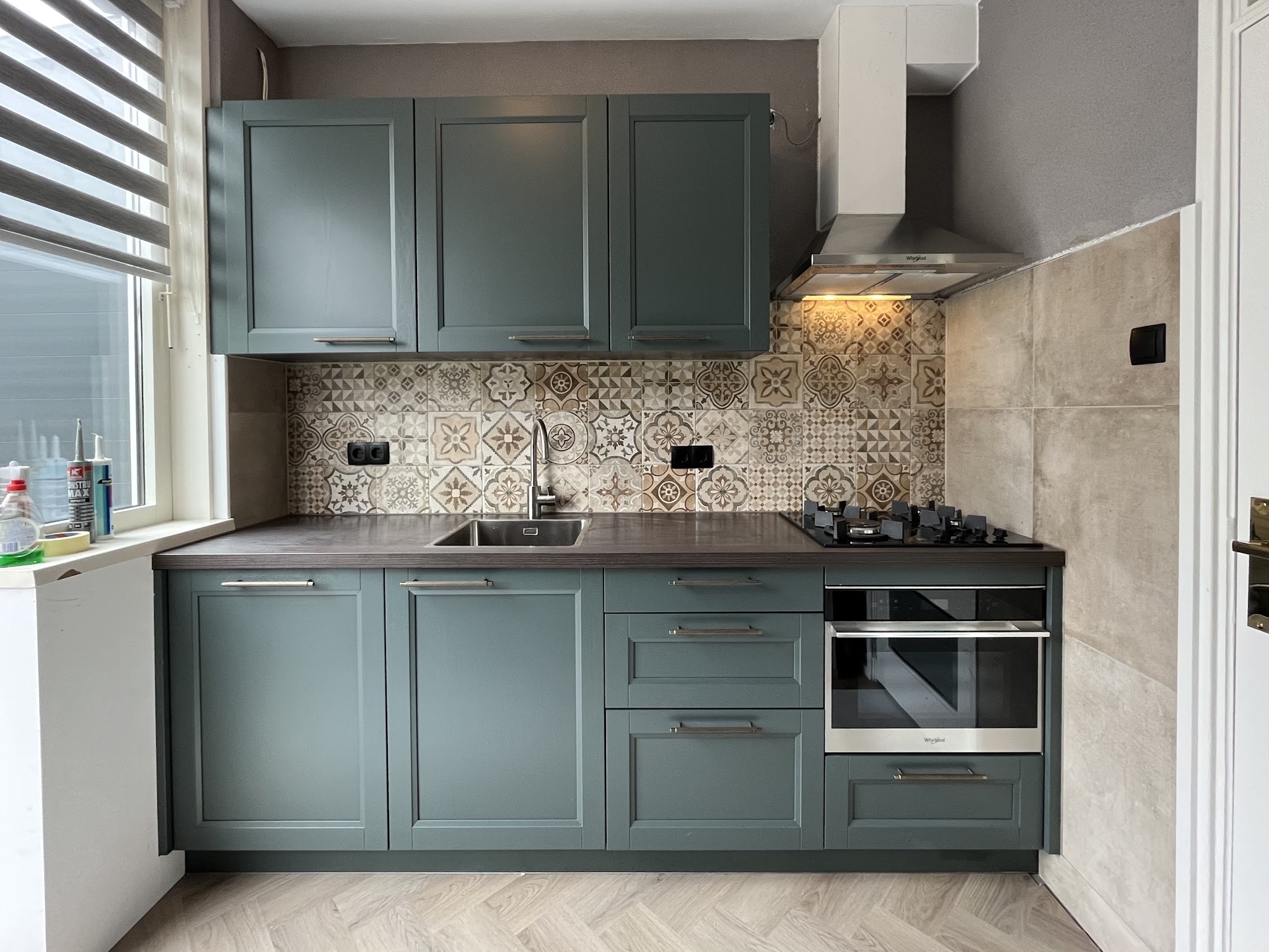 Geplaatste keuken met groene shaker fronten, patroontegels als achterwand en een donker houten werkblad
